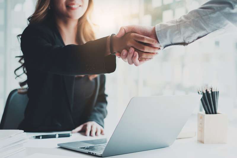 two people shaking hands over laptop comuter