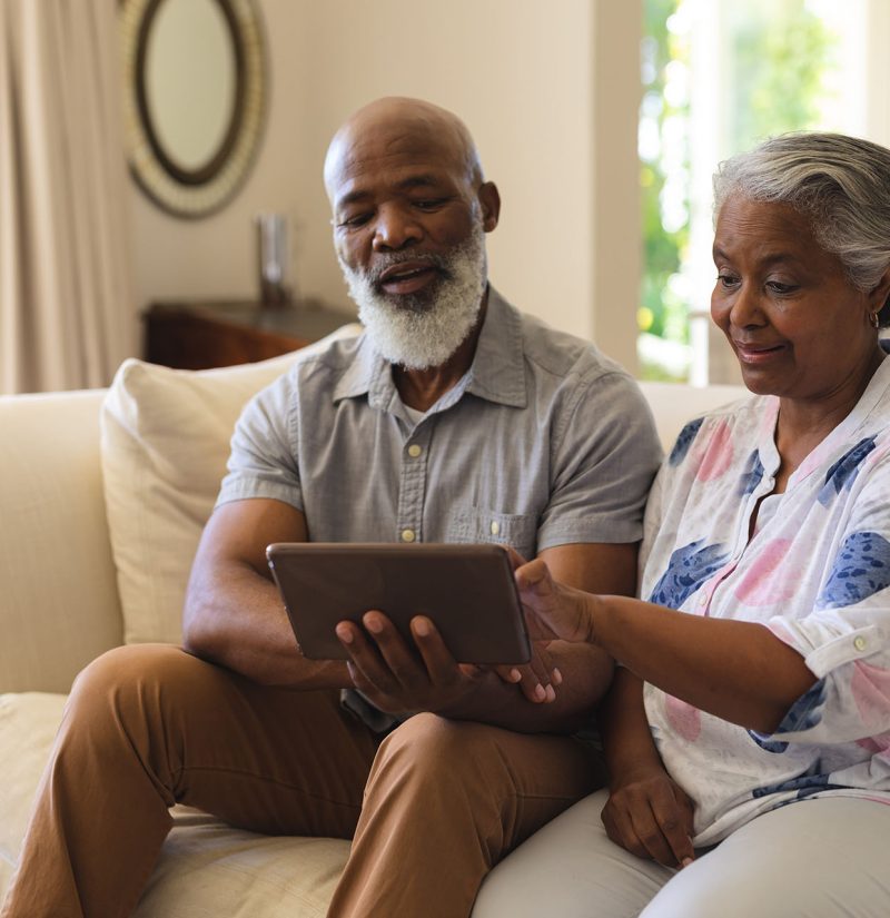 Senior african american couple sitting on sofa using tablet and smiling. retreat, retirement and happy senior lifestyle concept.
