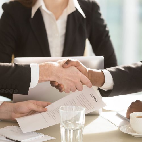Businesspeople shaking hands at negotiation table after singing contract.